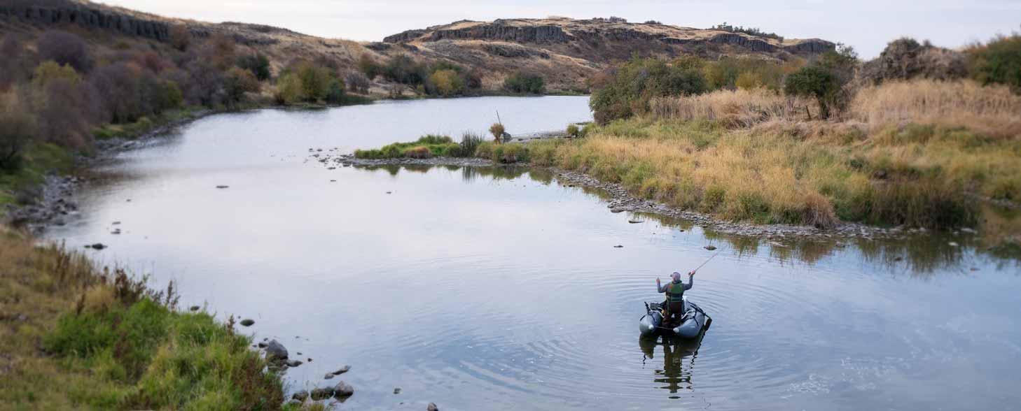 A fly fisherman casts from a lightweight NRS fishing raft in a western river.