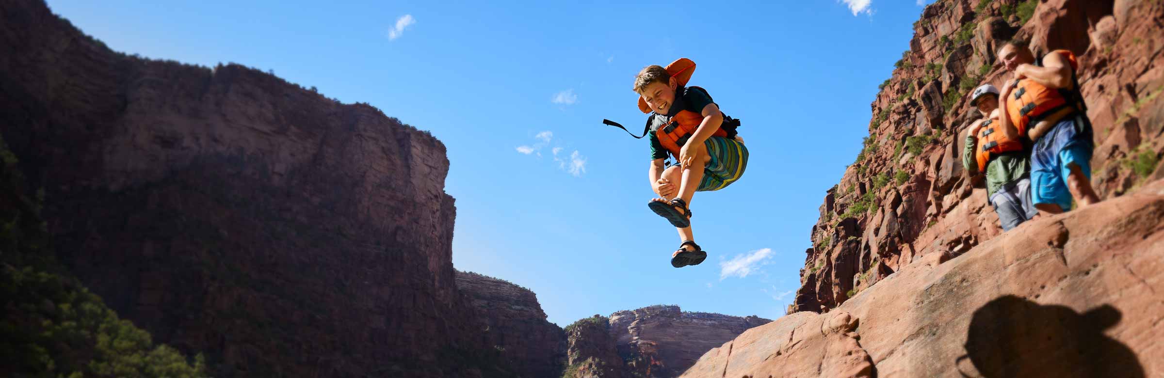 A child, wearing a life jacket, jumps into the river on a rafting trip.