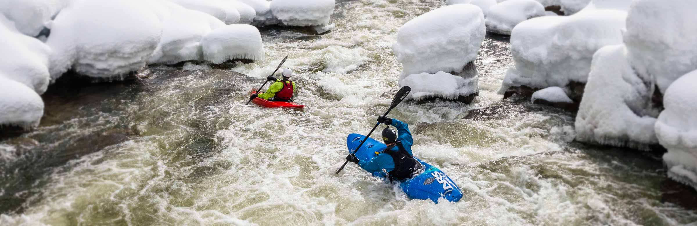 NRS kayakers heading downriver in the snow, dressed warmly for cold-water boating.