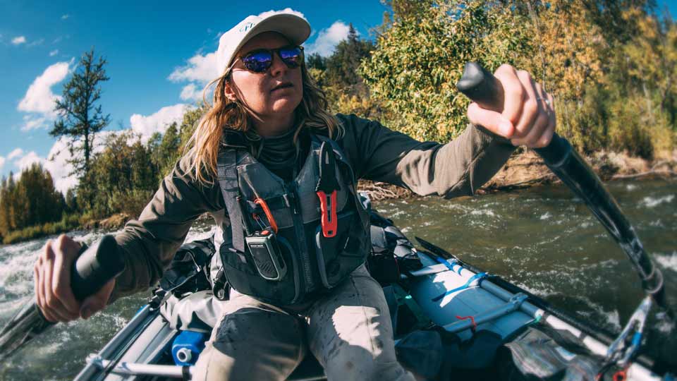 A woman rows a fishing raft wearing a fishing-specific NRS PFD.