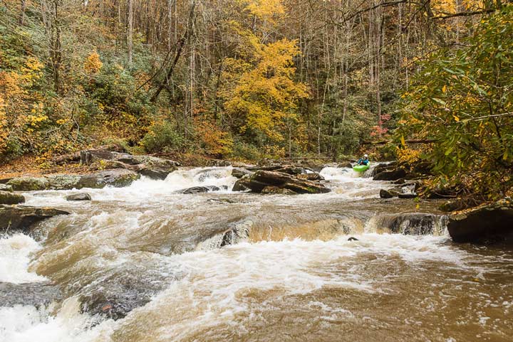 kayaker in river surrounded by trees with leaves changing colors