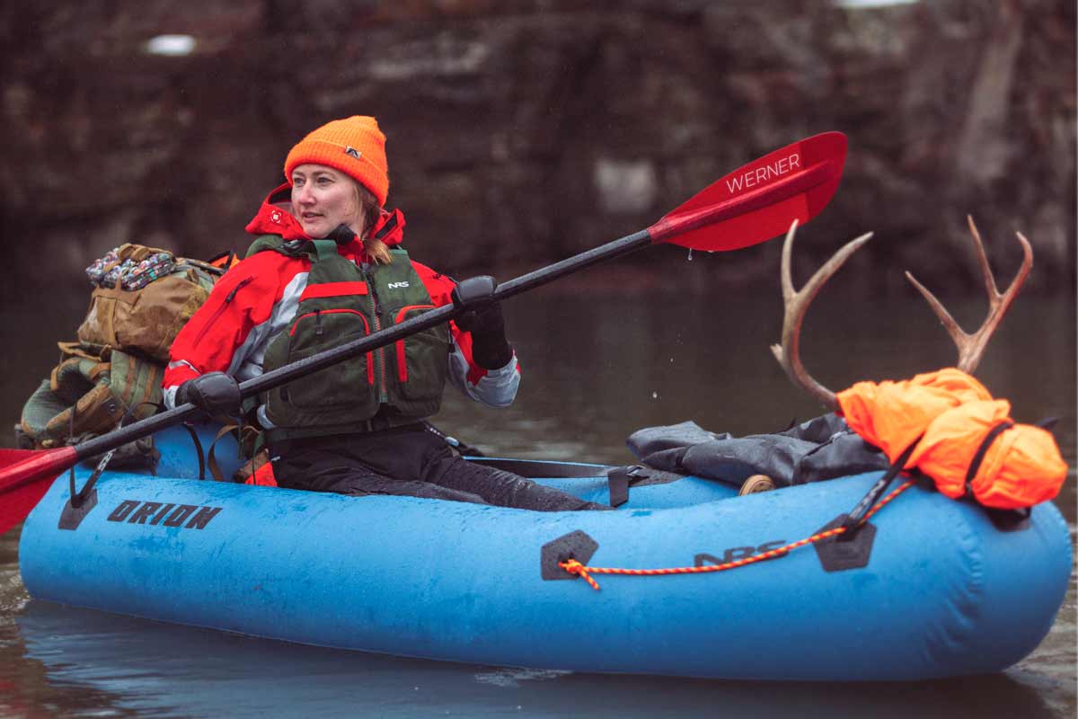 A woman in cold-weather hunting attire packrafts with a load of gear.