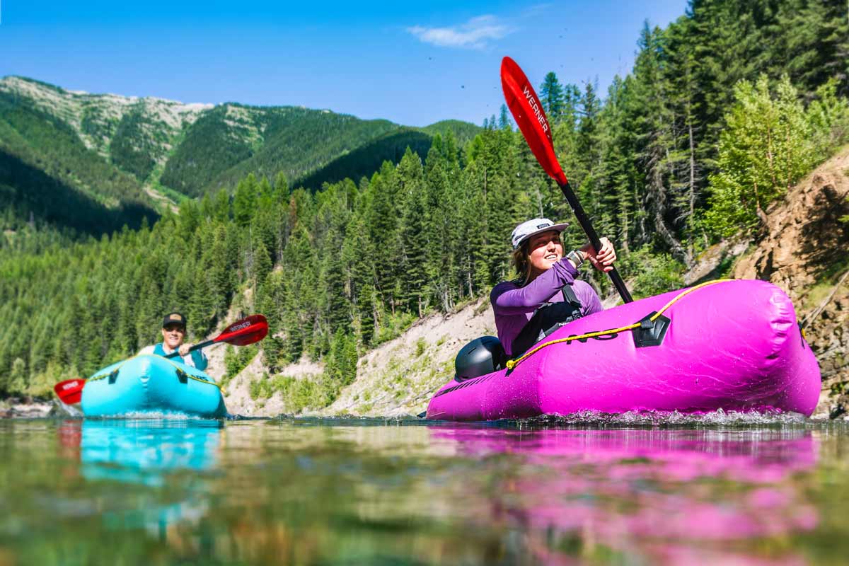 Two people paddle their NRS packrafts on calm mountain waters.