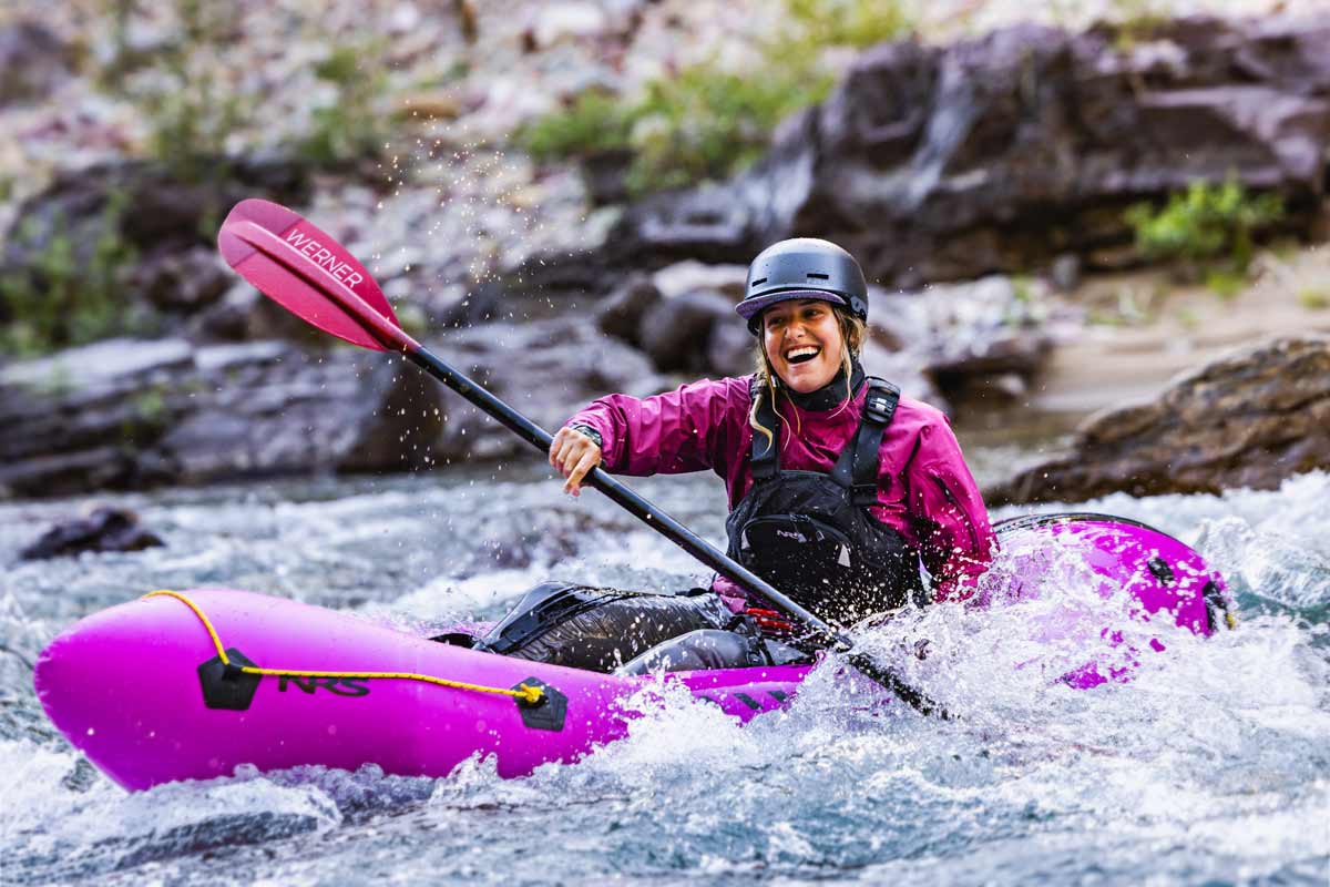 A woman happily maneuvers her packraft through whitewater.