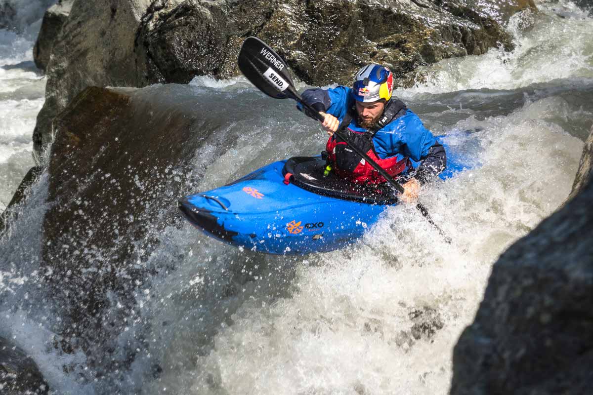 Paddler wearing the NRS Axiom GORE-TEX dry suit showing waterproof fabric and articulated paddling fit, goes over a waterfall in a kayak.