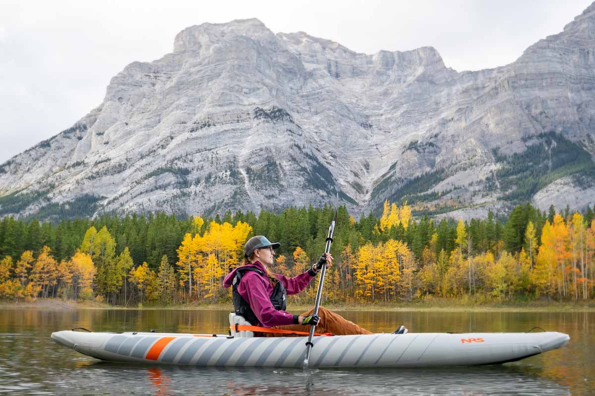With the mountains jutting out overhead, a woman eases through calm water in the Akamai 125 inflatable kayak.