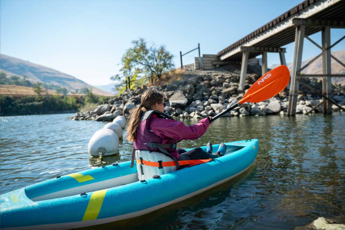 A woman heads towards a wooden bridge while paddling the Kaholo 110 inflatable kayak.