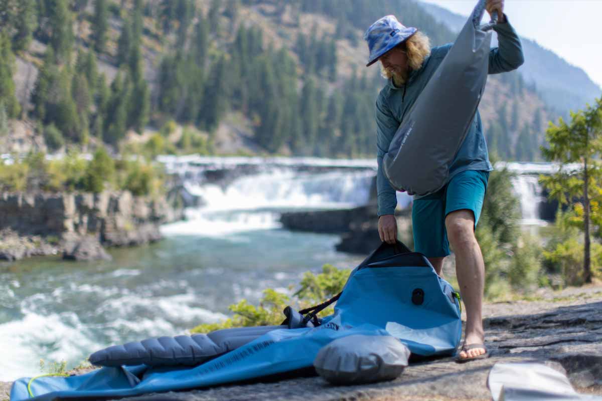 A man holds the NRS Packraft Internal Storage Bag preparing to stow it inside the Neutron SL Packraft.