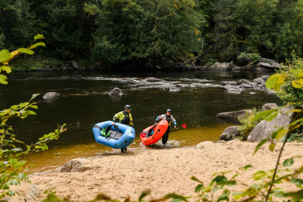 A couple carries their Neutron Packrafts up the sandy riverbank.