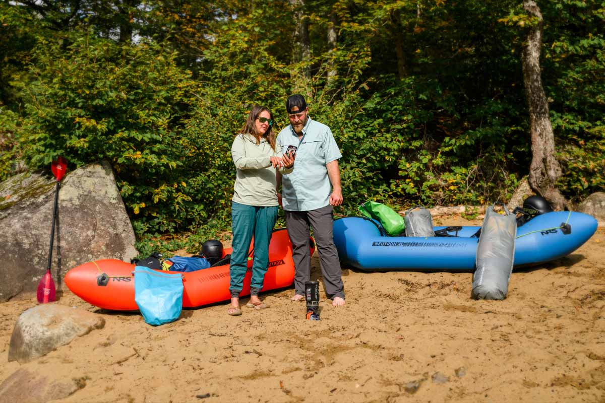 A man and woman stand together on the shoreline planning their route on the PaddleWays phone app.