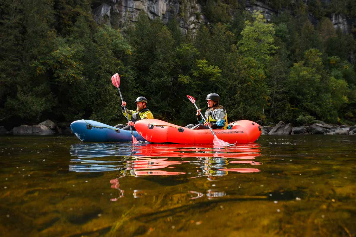 A couple leisurely paddle the NRS Neutron Packrafts down a calm river valley.