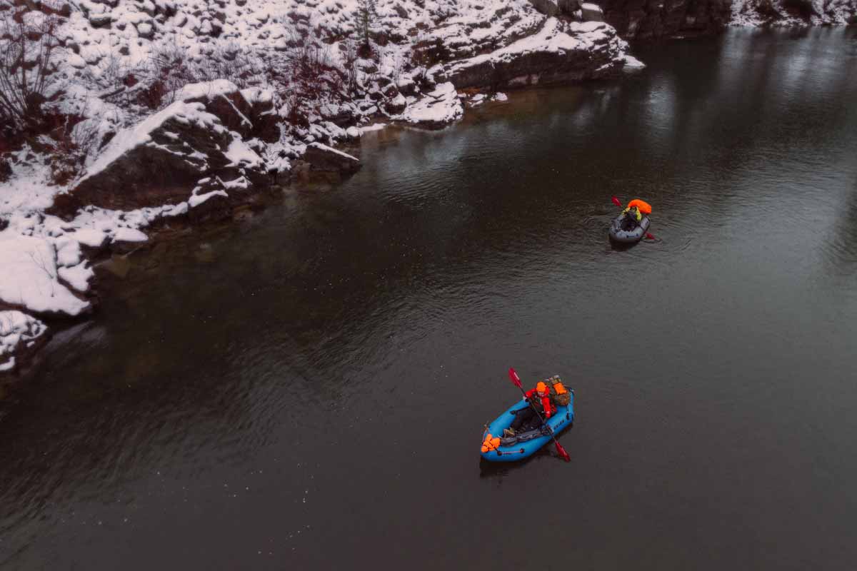 Two paddlers navigate down a wintry river in the Orio Packrafts.