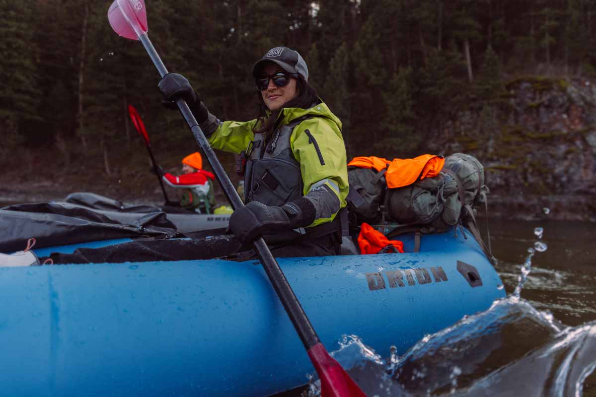 A woman paddles downriver in the Orion Packraft, fully rigged with hunting gear.