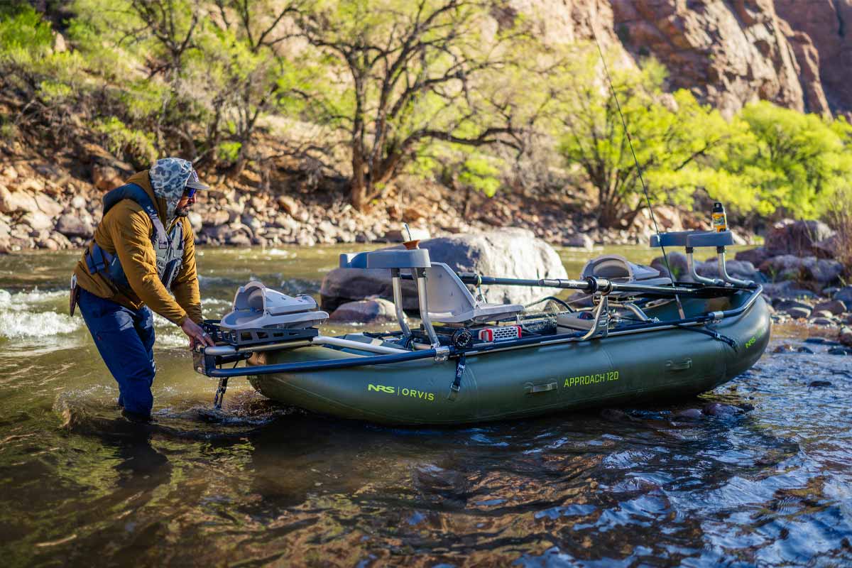 A man wades through a canyon river, pulling along the Orvis Approach 120 raft.