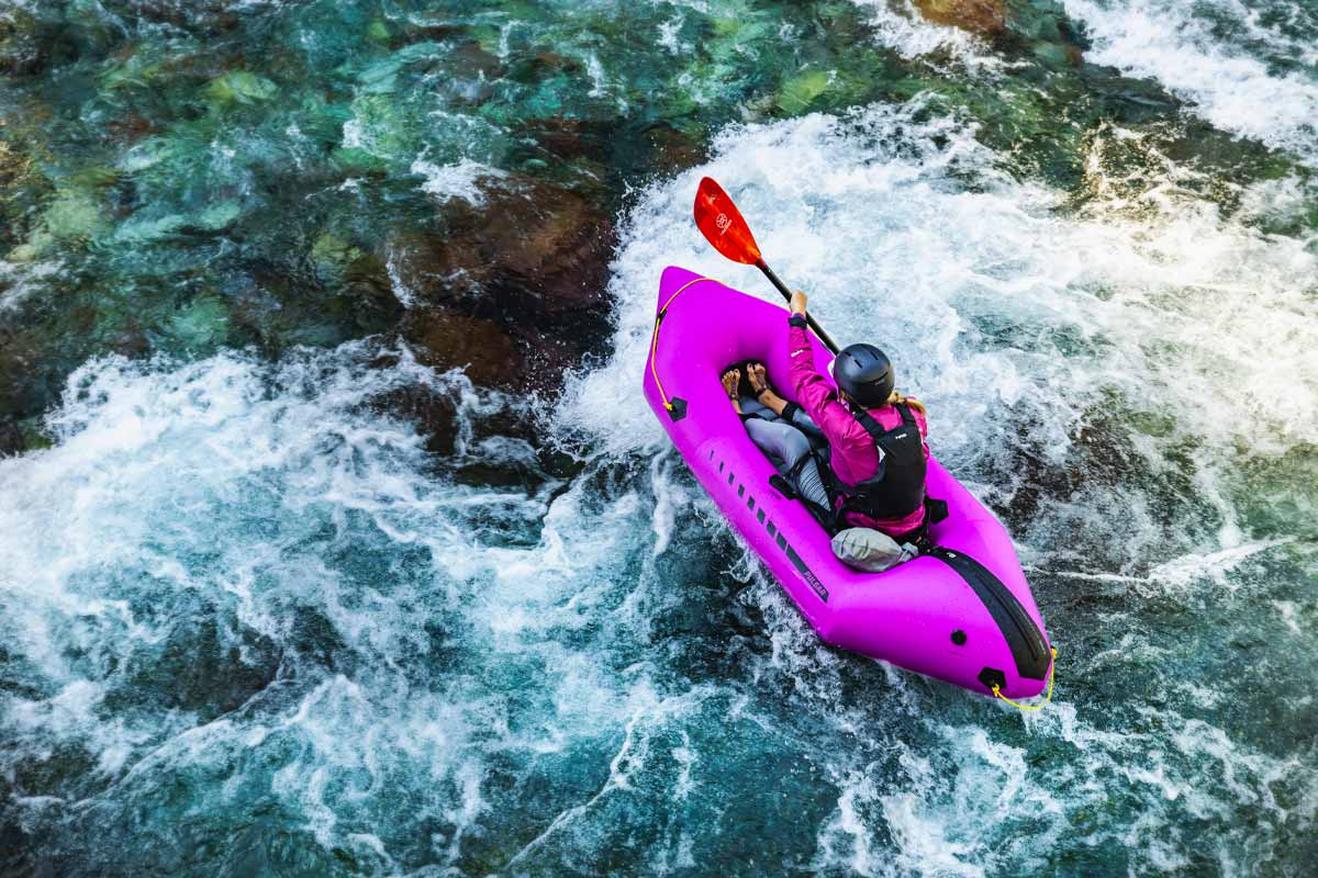 A woman charges through rapids while paddling the Pulsar Packraft.
