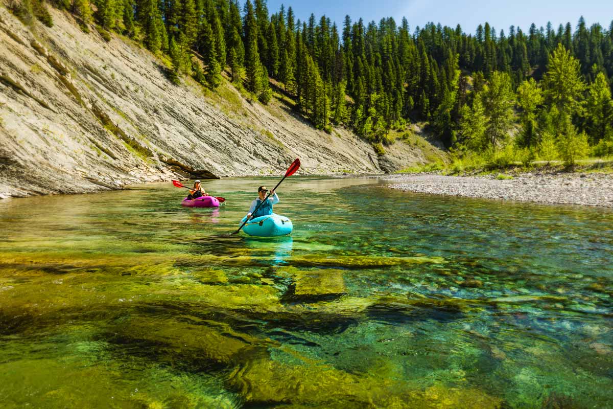 A couple leisurely paddles their Pulsar packrafts down emerald river waters.