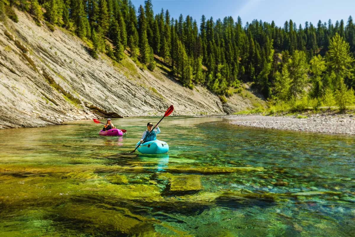 A couple leisurely paddles their Pulsar packrafts down emerald river waters.