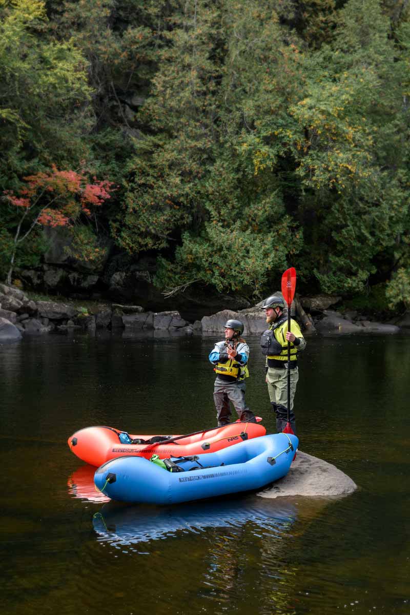 Man and woman stand on a rock in the middle of a river scoping out the best route.